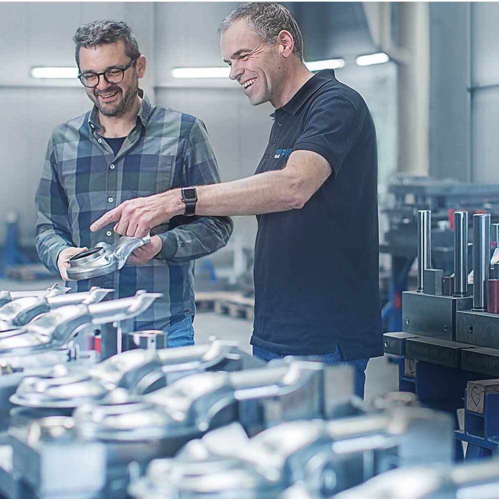 Two men looking at a set of workpieces made of metal.